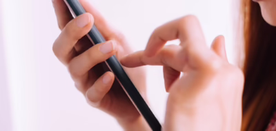 白背景でスマートフォンを使用する若い女性のアップ。