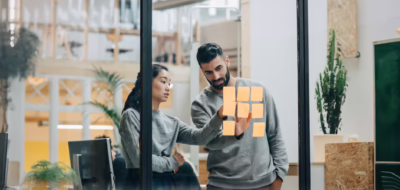 Homme d'affaires discutant avec une femme d'affaires collant des notes adhésives sur un mur en verre dans un bureau.